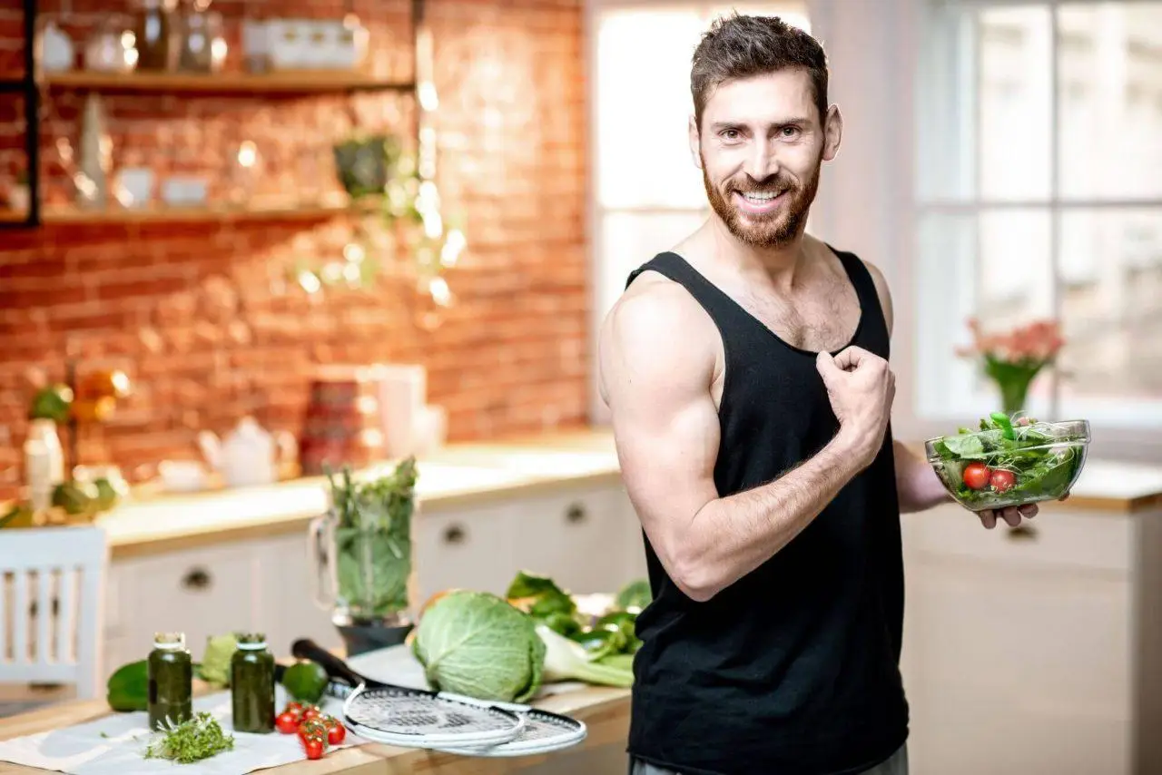 A handsome sports man showing muscles, eating healthy vegetarian salad on the kitchen at home