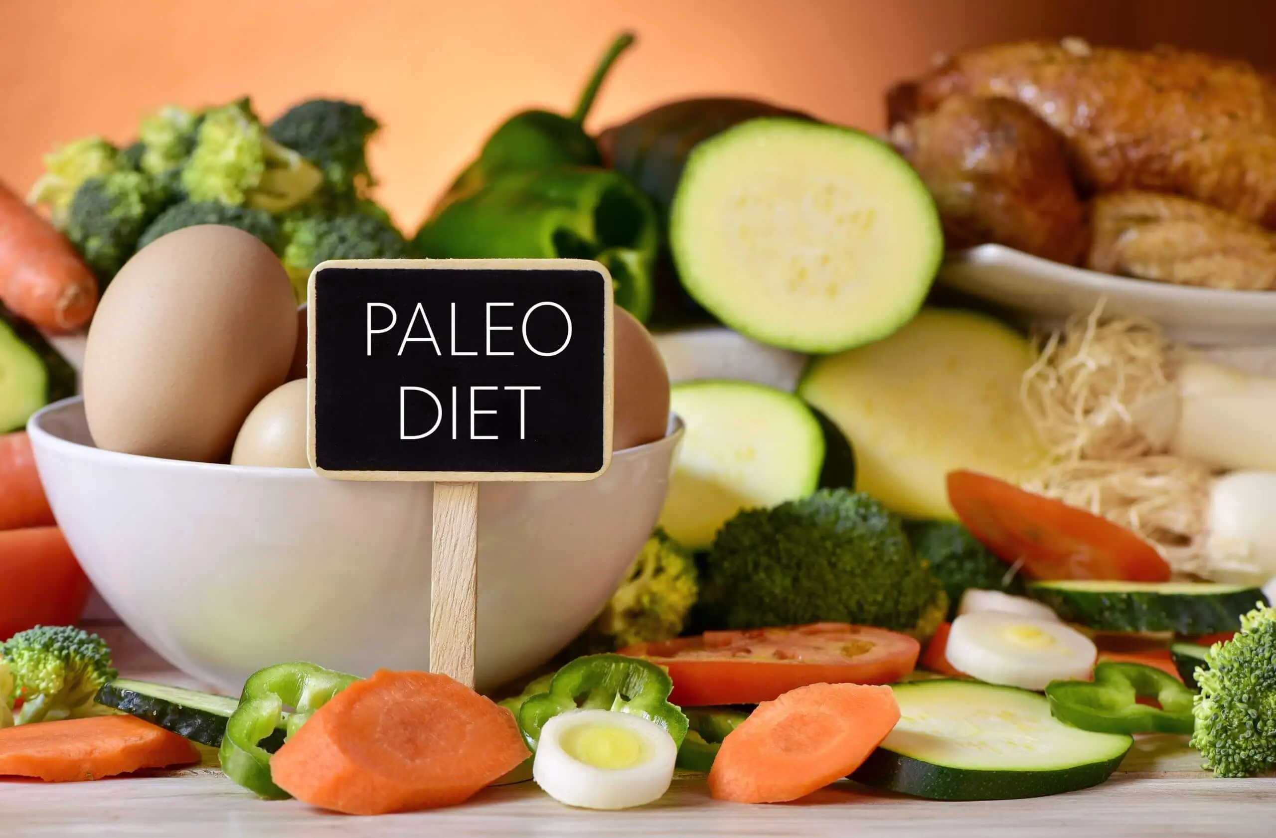 Paleo diet sign on a table full of various raw vegetables, a bowl of chicken eggs and chicken