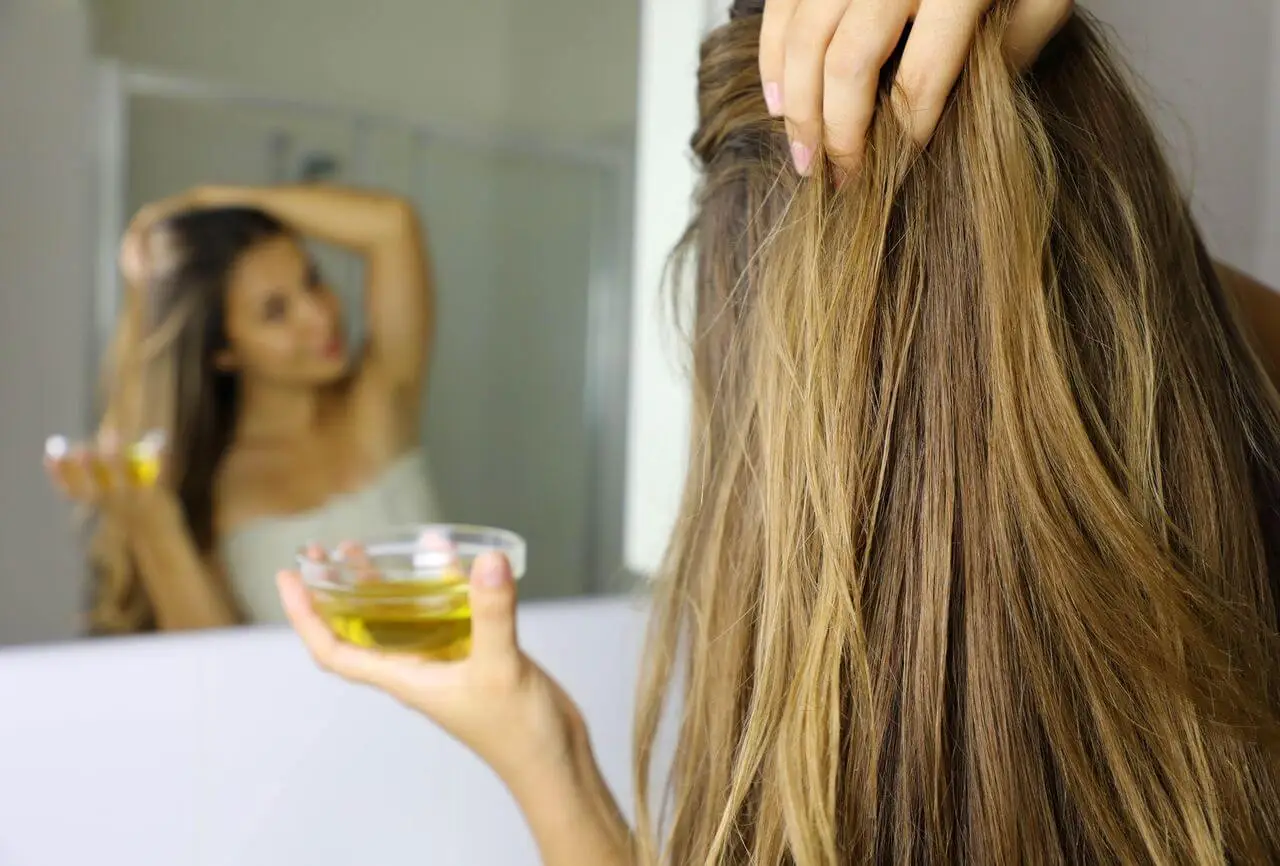 Young woman applying an oil mask on hair in front of a mirror