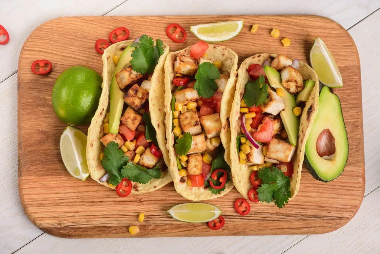 Yummy and crispy tacos with ingredients on a wooden cutting board