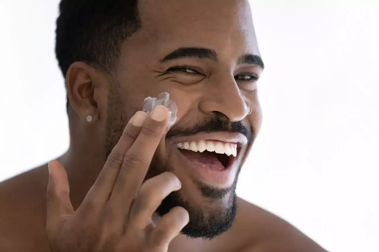Portrait of happy young african American man apply moisturizing face cream for healthy glowing skin