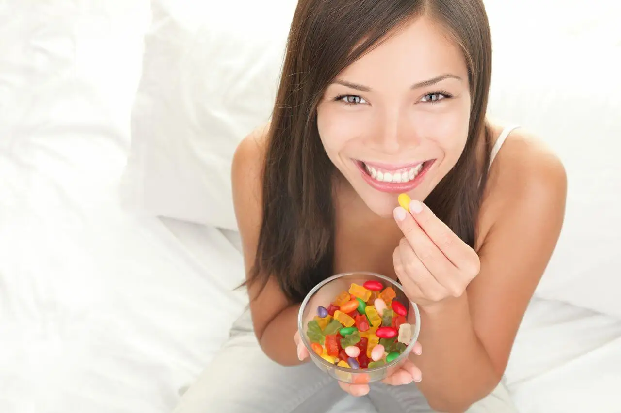 woman eating gummy sweets with a smile in bed